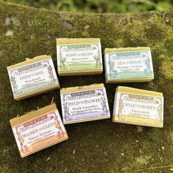 Assorted Old Factory Goat Milk Soap bars with different labels laid on a mossy surface.