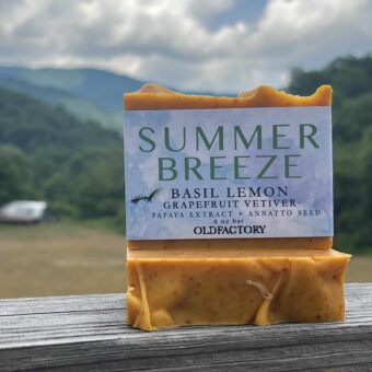Bar of orange soap resting on a wooden surface; label reads 'SUMMER BREEZE' with notes about basil lemon and grapefruit vetiver handmade by old factory soap hot springs north carolina